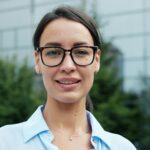 Portrait of a smiling young woman wearing glasses in an outdoor setting.